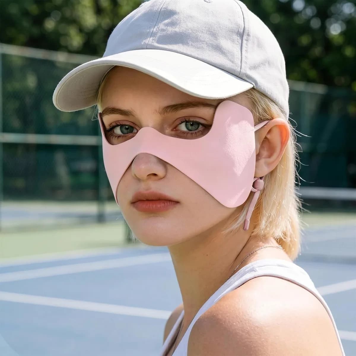 pink UPF 50+ sun face mask worn with a cap on a tennis court